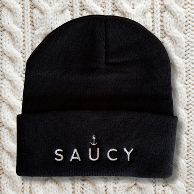 Black beanie with 'SAUCY' embroidery on a textured white background